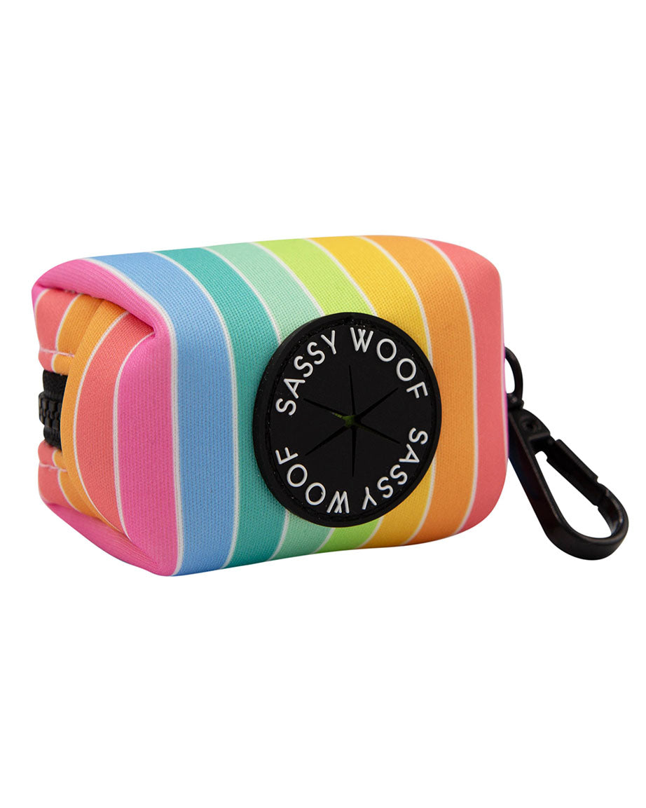 A SASSY WOOF Sassy Stripes pastel rainbow striped rectangular 3" pouch with black zipper and black clasp.  The rubber part where the waste bags come out in black and reads "SASSY WOOF" in white writing.