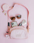 A build-your-own sassy woof example featuring pastel pink 2 compartment crossbody bag pouch, with a pastel pink and grey/gray strap and gold-toned clasp, attached near the top is a pastel pink 3.45" (inches) circular treat pouch. The photo shows how the crossbody bag can be used like a purse as well as a waste bag holder.