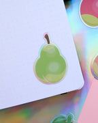 A holographic vinyl sticker shaped like an animal crossing new horizons pear stuck to a dot journal page.