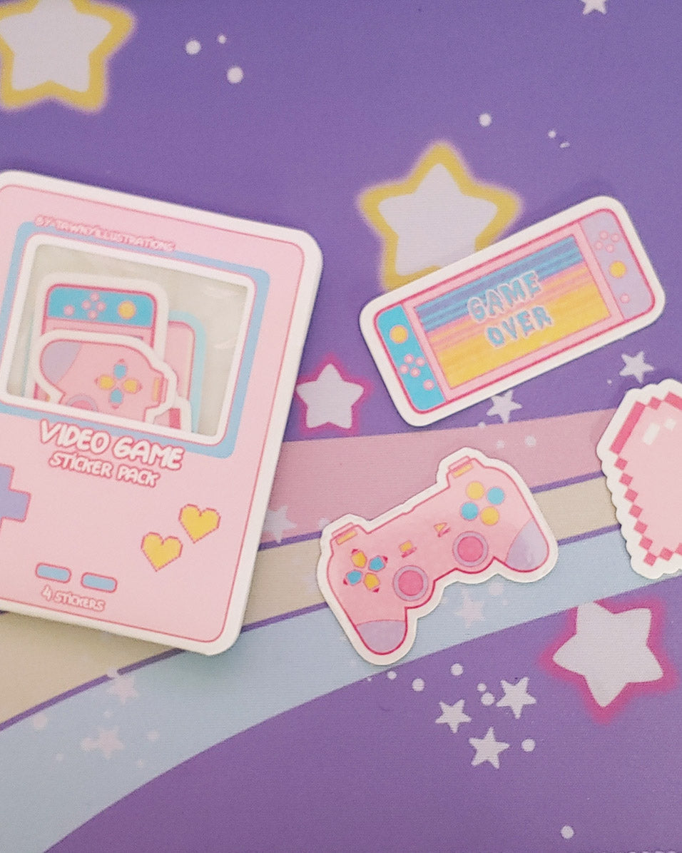Photo shows a full pack of the vinyl stickers inside the pastel pink game boy style packaging. On the right, there is a pastel pink, blue, and yellow nintendo switch that reads "game over", a pastel pink, blue, yellow, and purple playstation style gaming controller. Both stickers are vinyl.