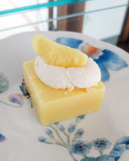 A yellow lemon scented cube with white whipped wax and a yellow lemon slice styled wax.  Non-edible.  Sitting on a white and blue floral plate.