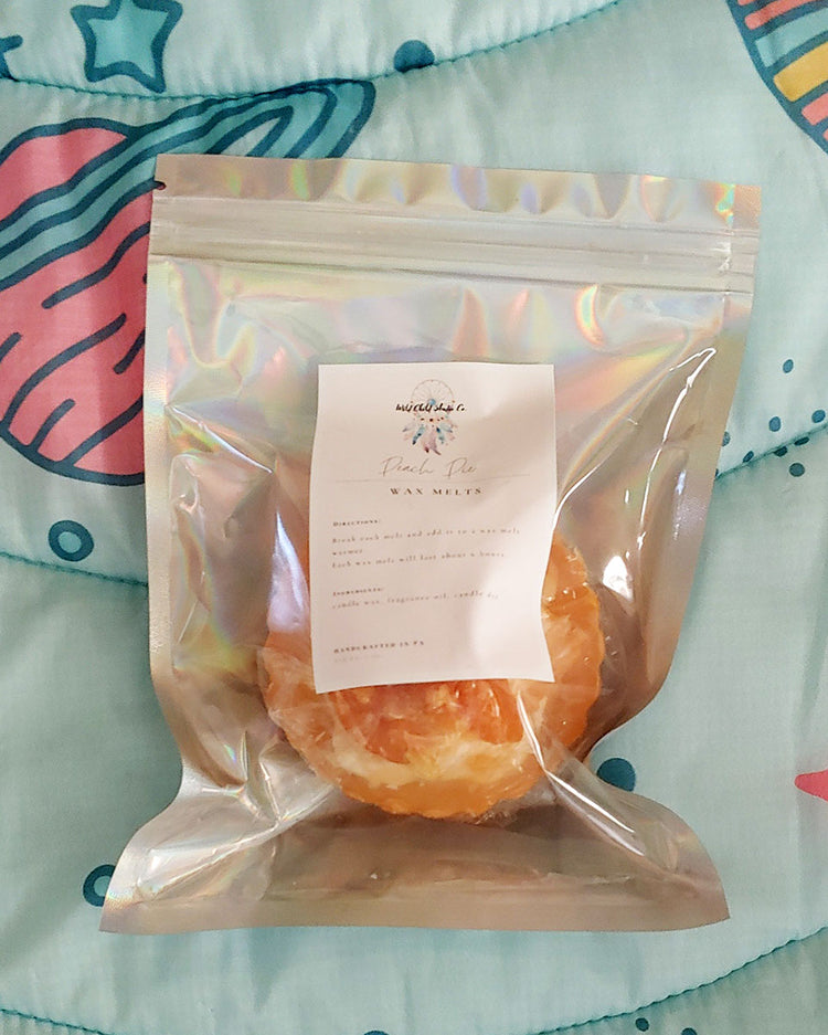 An orange and white max melt appearing to look like a peach pie with orange crust and white whipped cream with beautifully cute peach slices on top. It's shown inside its holographic pouch resealable packaging. Looks like a pie, but is not edible.