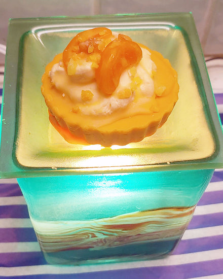 An orange and white max melt appearing to look like a peach pie with orange crust and white whipped cream with beautifully cute peach slices on top. It's shown on a green and brown art wax warmer. Looks like a pie, but is not edible.