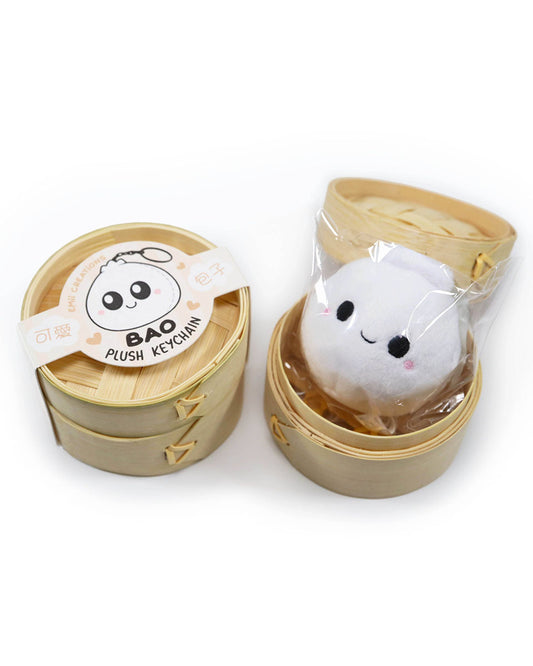 A cute kawaii smiling white bao keychain with rosy cheeks sits inside its open steamer packaging.