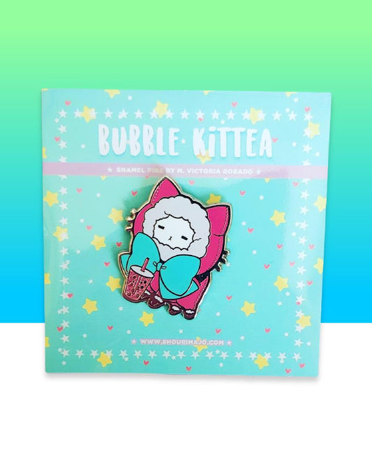 A white kitty cat in a hot pink sweater hoodie pull over with fur lined hood with a teal green giant bow.  The kitten is drinking a hot pink boba drink.  All of this art is on a had enamel pin and mint green "bubble kittea" backing card.