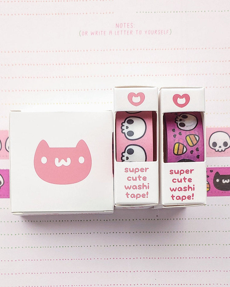 Adorable kawaii black and white skulls on a coral pink washi paper tape.  Sitting next to black and white kawaii skulls with black hearts and yellow , orange, and white candy corn on a fuchsia (pinky purple) washi paper tape that is also available in our store