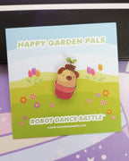 A cute kawaii pug dog with a de-potted plant on its head. It's hiding/sitting in a pink plant pot. A hard enamel lapel pin.