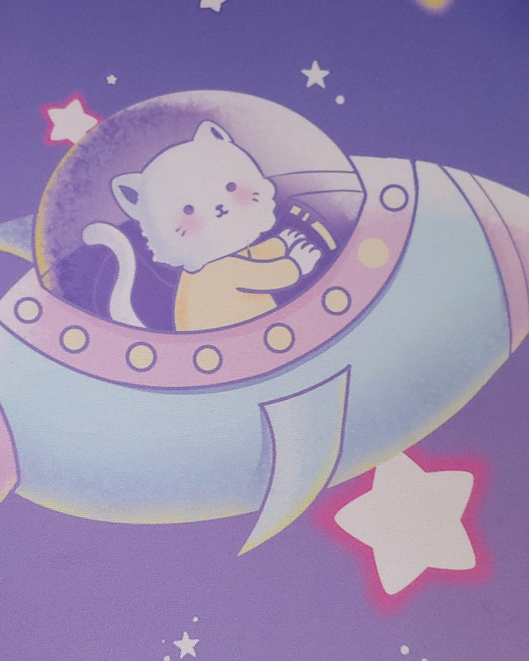 A little white blushing fluffy kitty with a yellow shirt commands a pastel yellow, pink, and blue space ship. The space ship is surround by a purple sky with white stars.  Some stars are outlined with hot pink and others with gold.