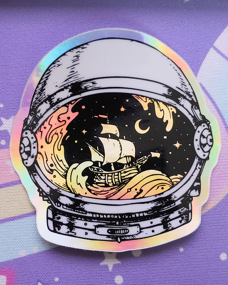 A white and black holographic astronaut helmet vinyl sticker with visions of a sail boat setting sail on the sea at night with the moon in the background.