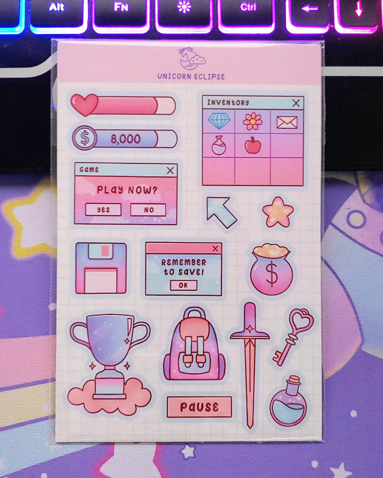 An adventure planner sticker sheet with 15 stickers featuring a health points meter in pink, a money tracker in blue, a play now gaming window, a floppy disk, a remember to save window, an arrow, a yellow star, a purple, pink, and yellow pot of gold with money symbol on it, a blue, purple, pink, and coral trophy, a pink, purple, blue, and coral backpack, a coral pause rectangle, a pink and coral sword, a pink heart key, and a blue and purple mana potion.