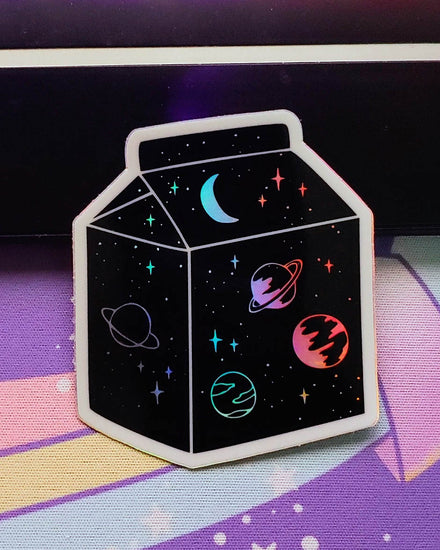 A black, white, and holographic vinyl sticker featuring a milk carton filled with space...outer space that is...there are stars, a crescent moon, jupiter, saturn, and other planets.