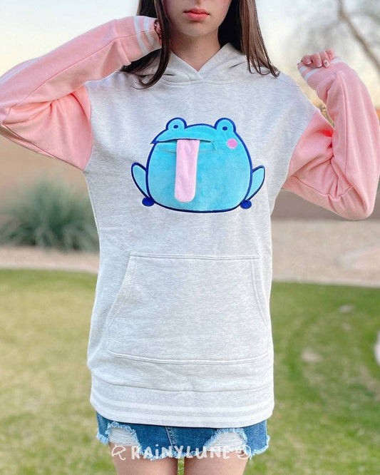 A grey/gray hoodie sweatshirt dress with pastel pink sleeves with two white stripes on the cuff. The design consists of a mint green frog lined with navy blue. The frog is has pink cheeks and a zipper mouth. If unzipped and pink tongue can be pulled out and the frog now is sticking out its tongue.