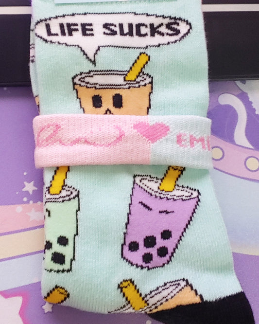 Yellow, purple, and green pastel kawaii boba socks. Reads "Life sucks." Happy and sad faces on mint colored socks with black toes and heels.