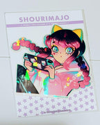 A pink and black gradient/ombre haired girl with pigtails and a pink, white, and blue pastel track jacket and black and blue track pants sits and leans back while playing her blue and black nintendo switch that is covered in kitty cat stickers.  She has blue and yellow cat ears on and yellow eyeshadow her eyes sparkle. All of this digital art piece is printed on a broken glass holographic vinyl sticker.  Attached to a white card with brand name and purple stars.