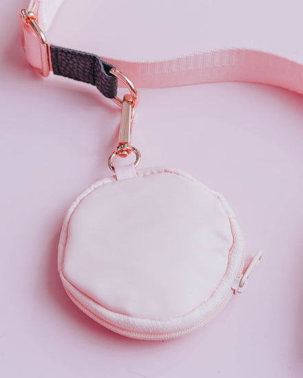 A pastel pink circular pouch measuring about 3.45" (inches) with gold toned clasp attached to a pastel pink and dark grey/gray strap to show example of the build-your-own style of the doggy crossbody set.