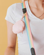 A pastel pink 3.45" (inches) circular treat pouch attached to a sassy stripes pastel rainbow with black details and gold-toned clasps worn by platinum blonde model with a v-neck white t-shirt.