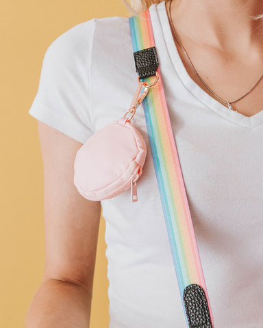 A pastel pink 3.45" (inches) circular treat pouch attached to a sassy stripes pastel rainbow with black details and gold-toned clasps worn by platinum blonde model with a v-neck white t-shirt.
