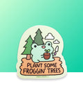 A cute kawaii smiling frog froggie holding a gardening spade and a plant with dirt and a leaf sitting in camp dirt with two pine trees behind him and two clouds in the sky on a vinyl sticker. The sticker reads "Plant some froggin' trees." Designed by small business robot dance battle