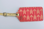 A pleather luggage tag with pink tag and gold-toned foil arrows.  Stitched together and gold-toned strap.